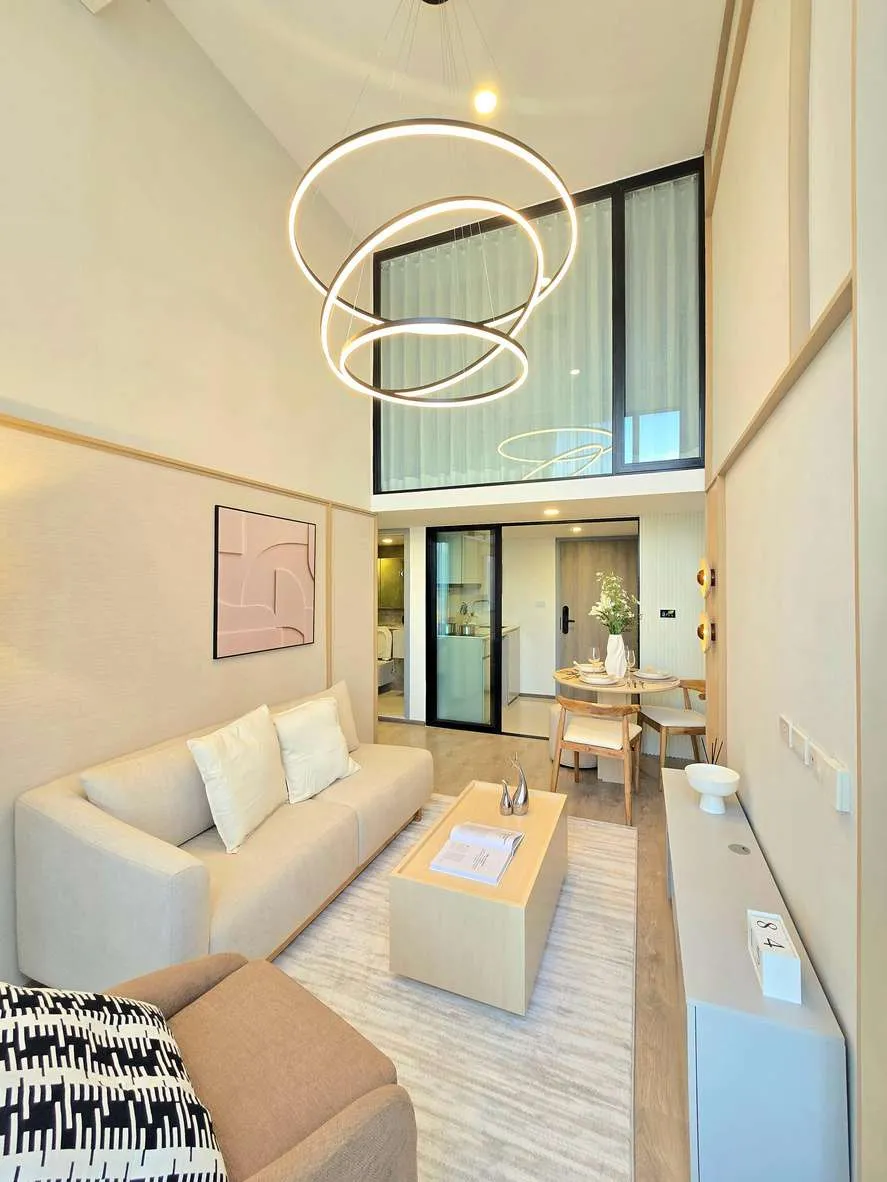 Finished double-height living room with a ring chandelier, cream sofa and tall windows